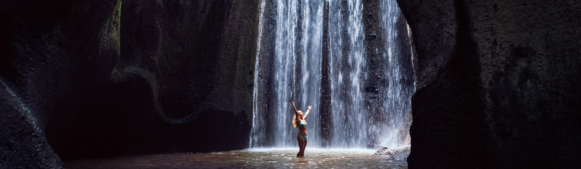 A lady in her swimwear rejoicing at the bottom of Tukad Cepung Waterfall, Bali